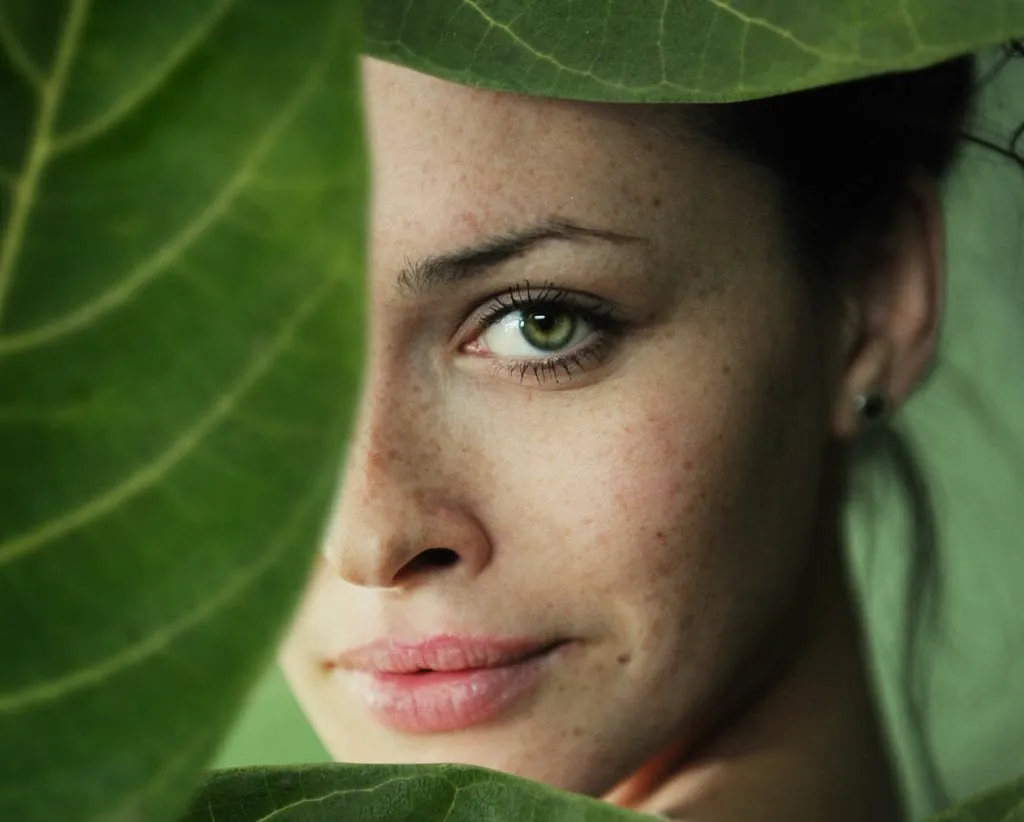 Mujer con pecas asomando tras una hoja verde